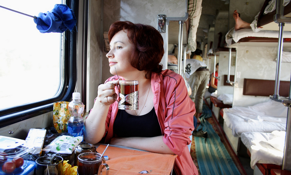 Женщина в розовом кардигане сидит с чашкой чая в плацкартном вагоне