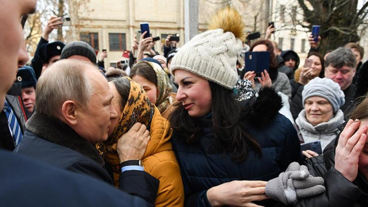 Девушка в синем пуховике и серой шапке улыбается на улице президенту Владимиру Путину