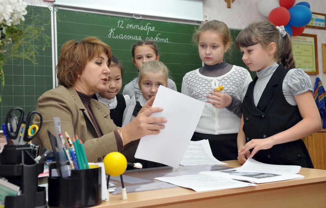 Пятеро школьниц слушают объяснения у стола учителя