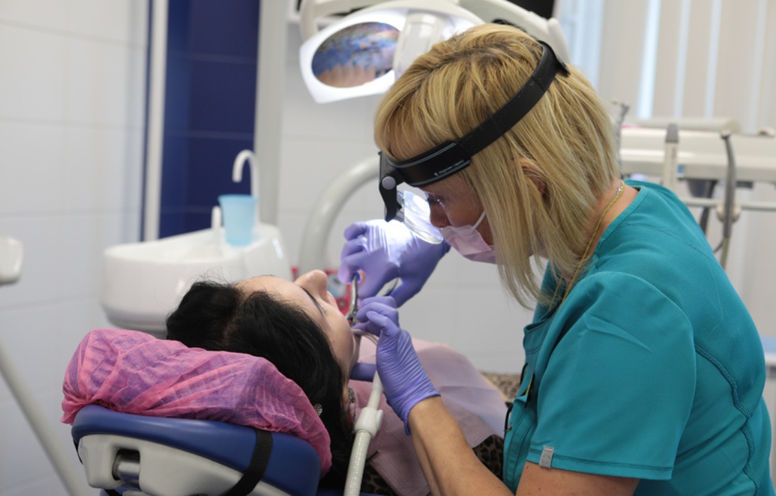 Стоматолог в зеленом халате лечит зуб пациенту